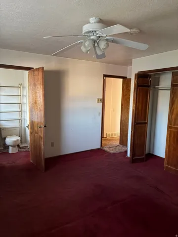 Ceiling fan with integrated lighting, wood-finish interior doors, built-in closet with bi-fold wood doors, wall-mounted towel rack, and a ceramic toilet fixture