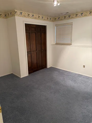 Recessed window with blinds, dark wood-paneled bi-fold closet doors, wall-mounted track lighting, and blue carpeting