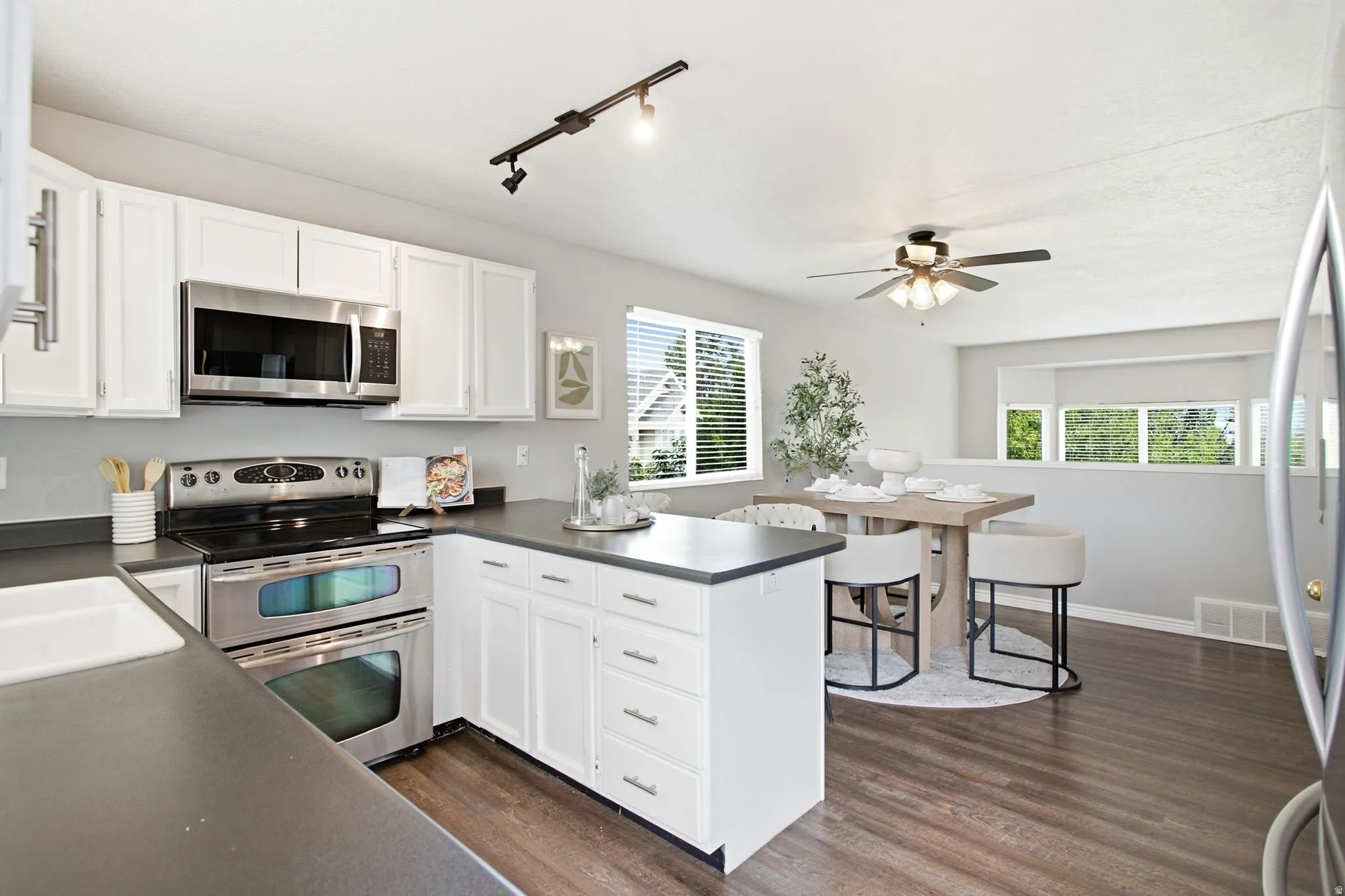 White cabinetry with stainless steel hardware, track lighting, stainless steel double oven range, stainless steel microwave, and wood-finish flooring