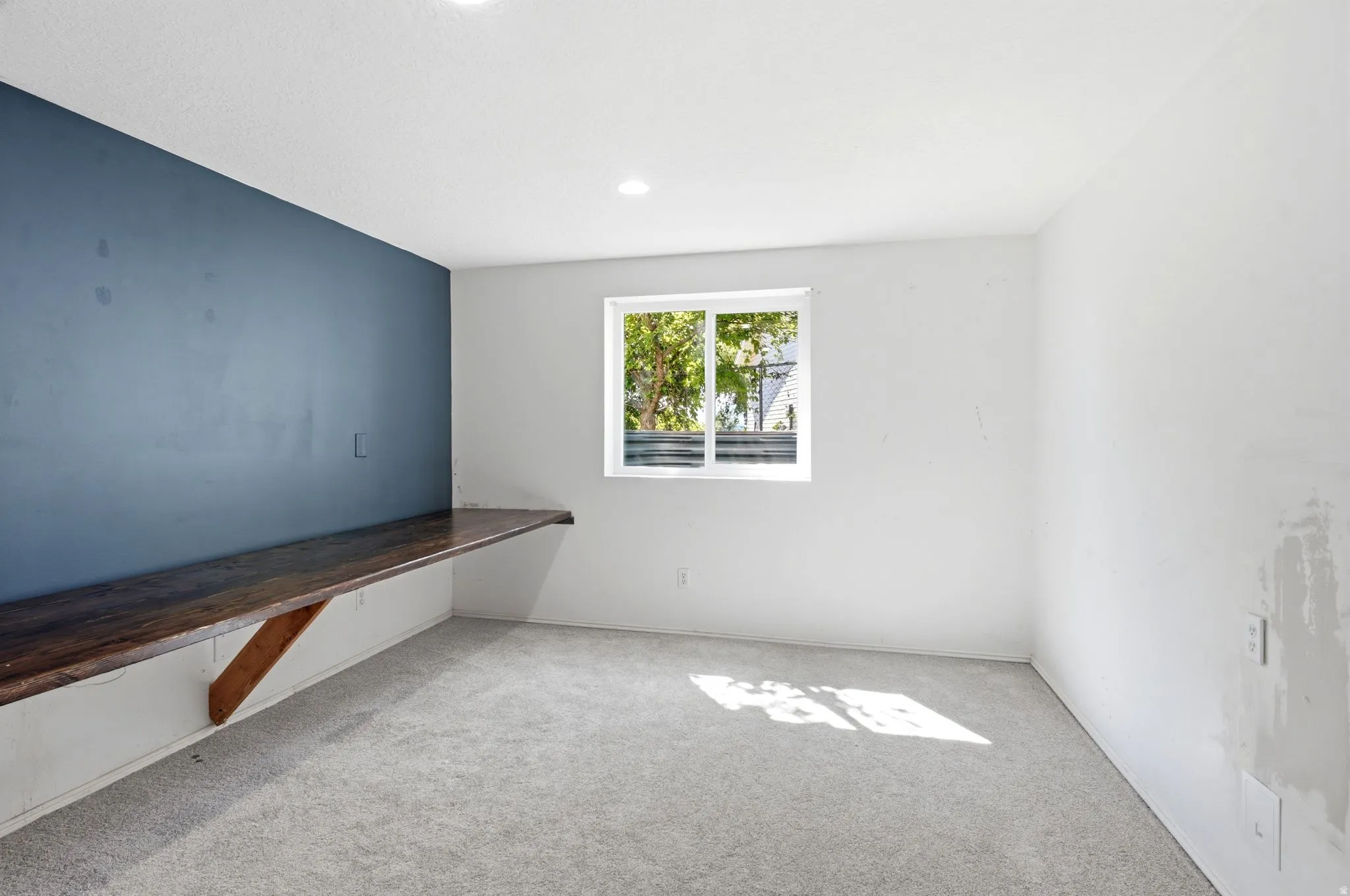 Room featuring a built-in wood-finish desk, recessed ceiling lighting, a window with white trim, and light gray carpeting