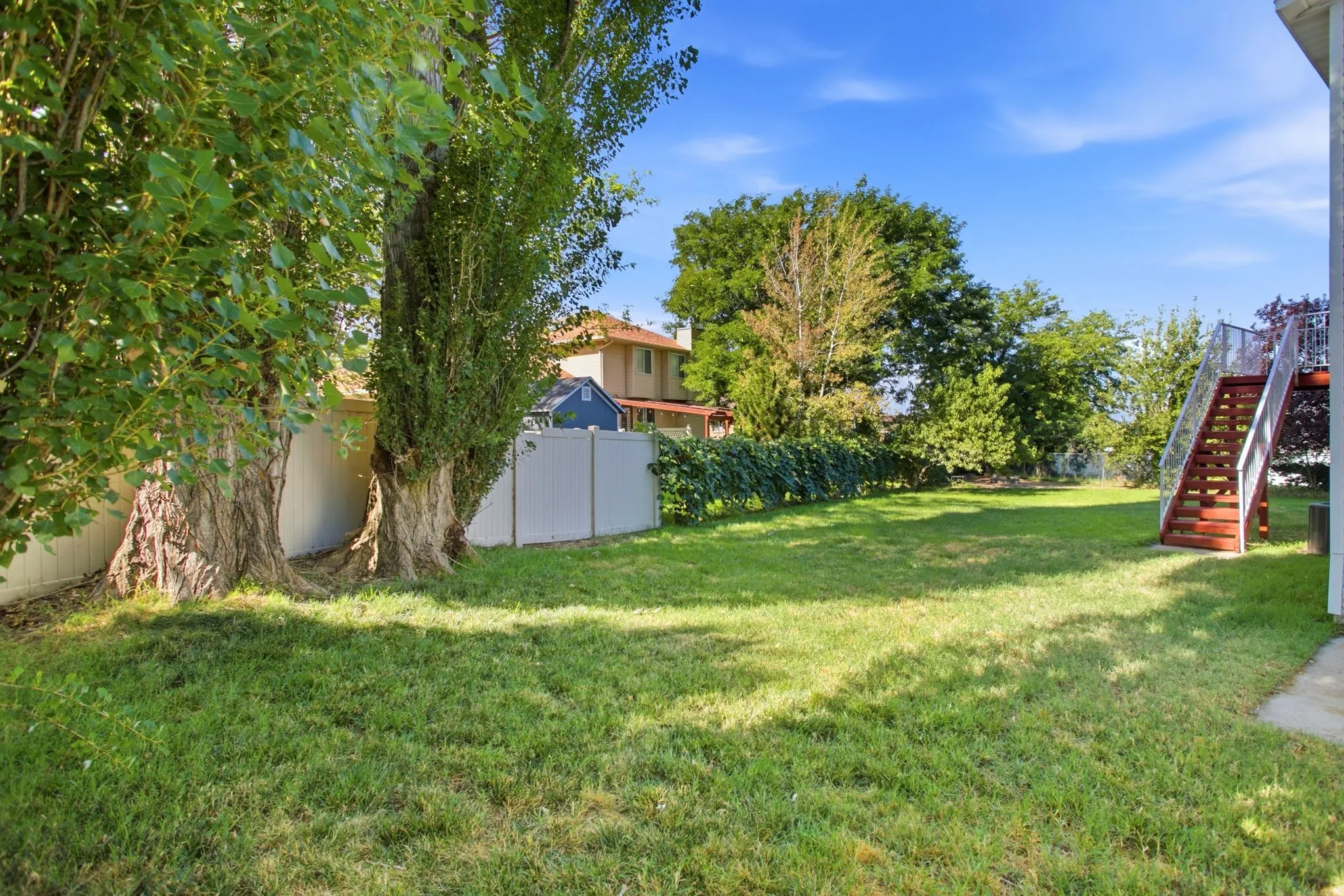 Expansive grassy yard with mature trees, privacy fencing, and exterior stairs with wood-finish treads