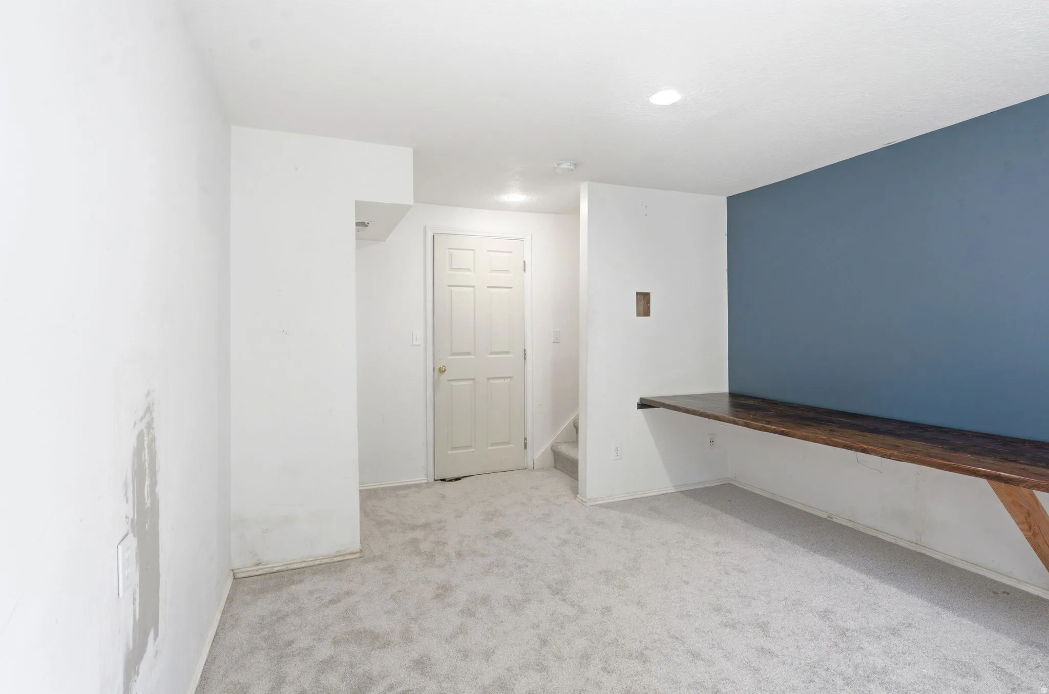 Lower level room featuring light gray carpeting, recessed lighting, a built-in wood-finish desk, and a contrasting accent wall