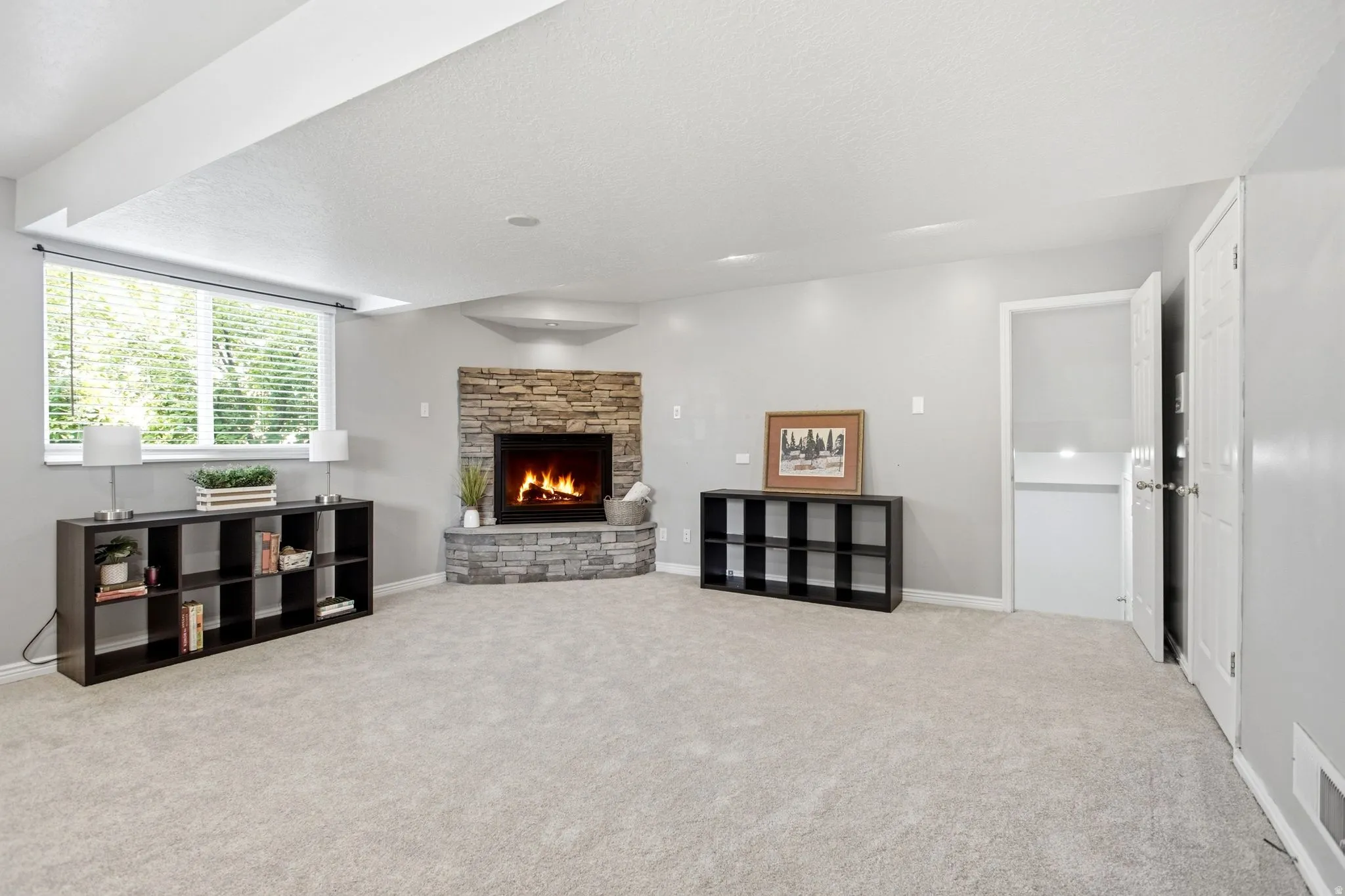 Corner fireplace featuring a stone surround and hearth, neutral carpeting, window with horizontal blinds, and recessed lighting