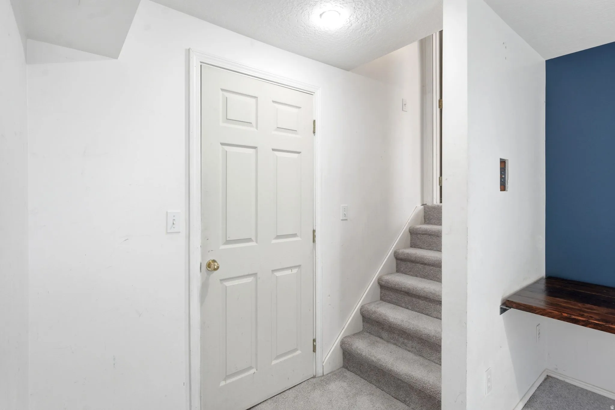 White paneled door with brass hardware, carpeted staircase, recessed lighting, built-in wooden bench, and accent wall
