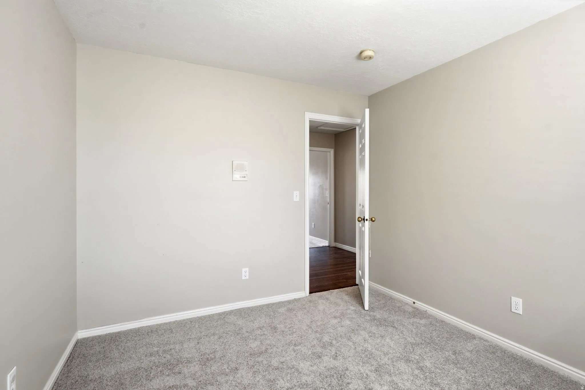 Room featuring light gray wall paint, gray carpeting, white baseboards, and a standard door with a brass knob