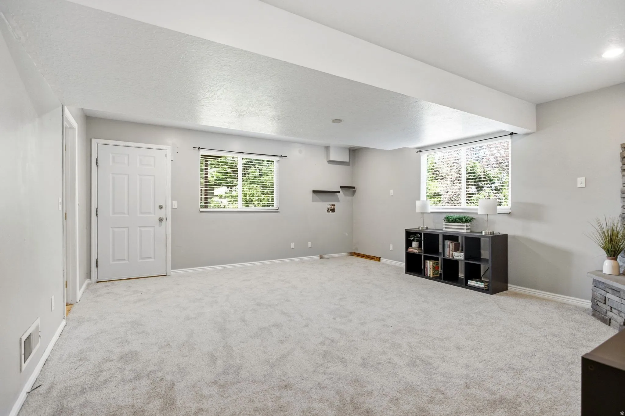 Bright, open recreation room featuring neutral carpeting, abundant natural light from multiple windows, white painted walls, and built-in shelving