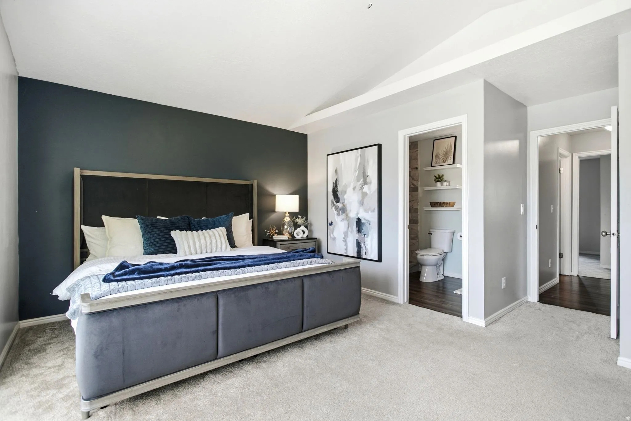 Vaulted ceiling, plush carpeting, dark accent wall, recessed lighting, and interior access to a bathroom with built-in shelving