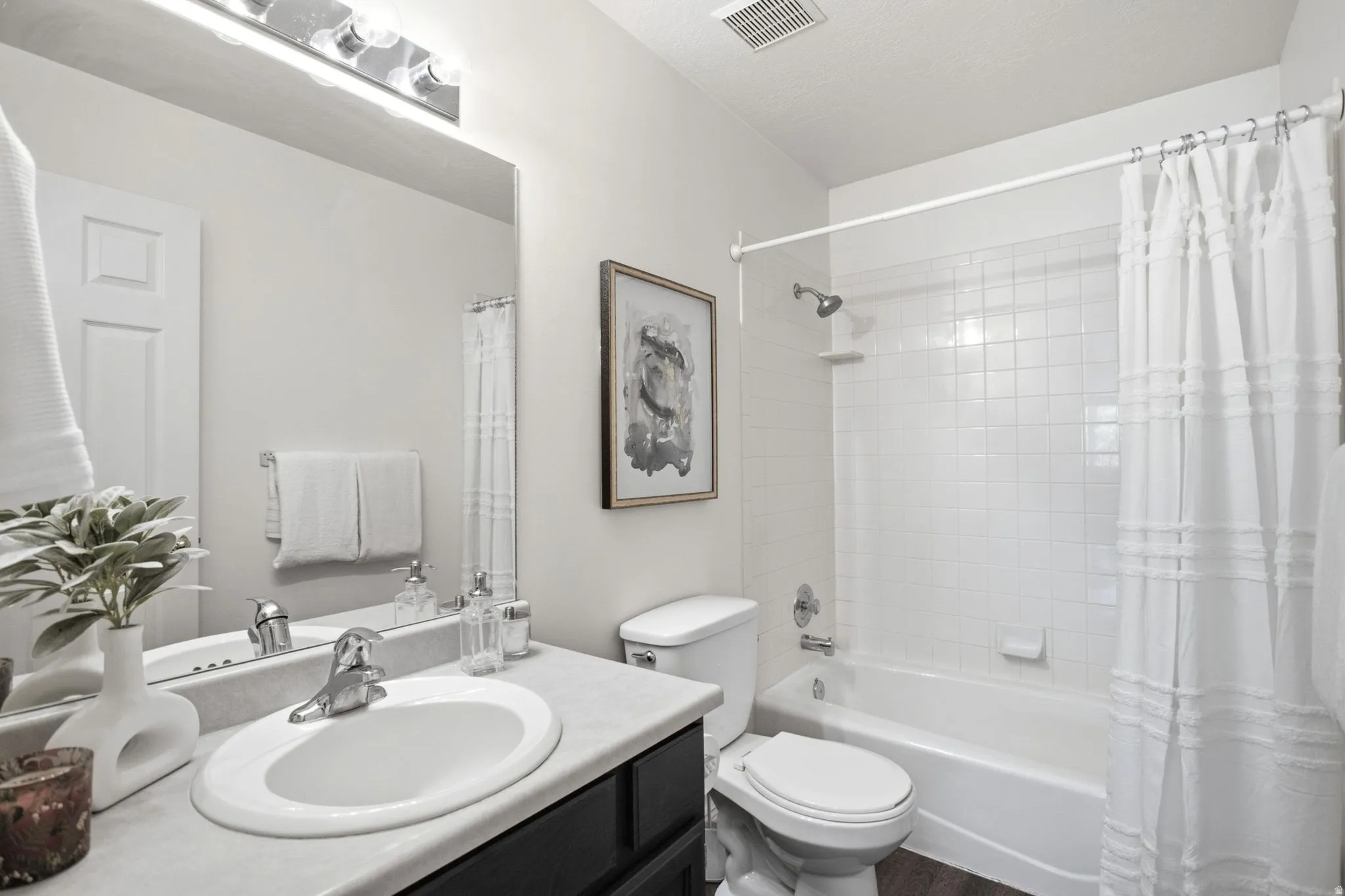 Bathroom featuring a vanity with an oval sink, chrome faucet, wall-mounted mirror, overhead lighting, and a white tiled shower-tub combination