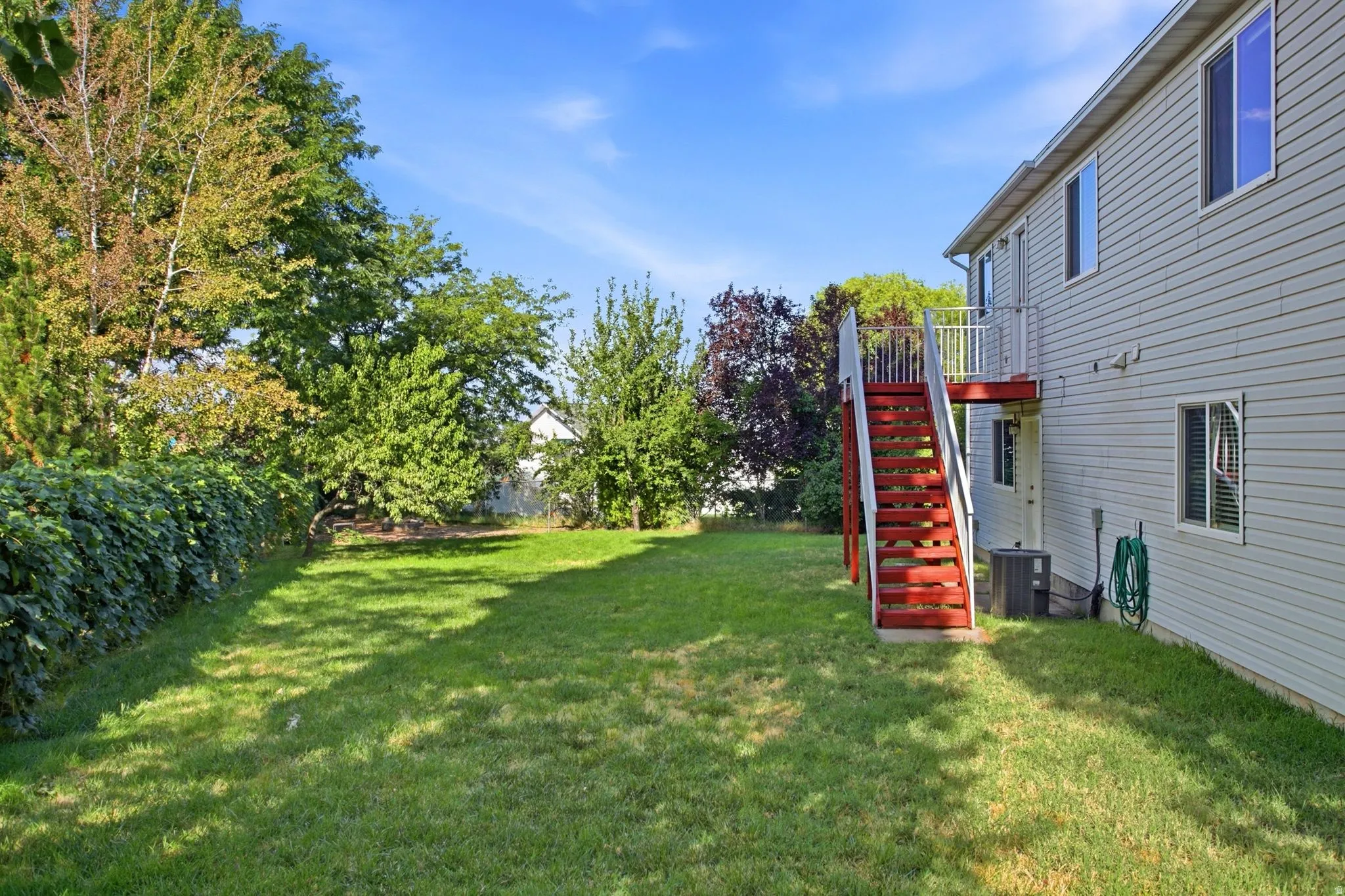 Expansive backyard with a manicured lawn, established landscaping, and mature trees