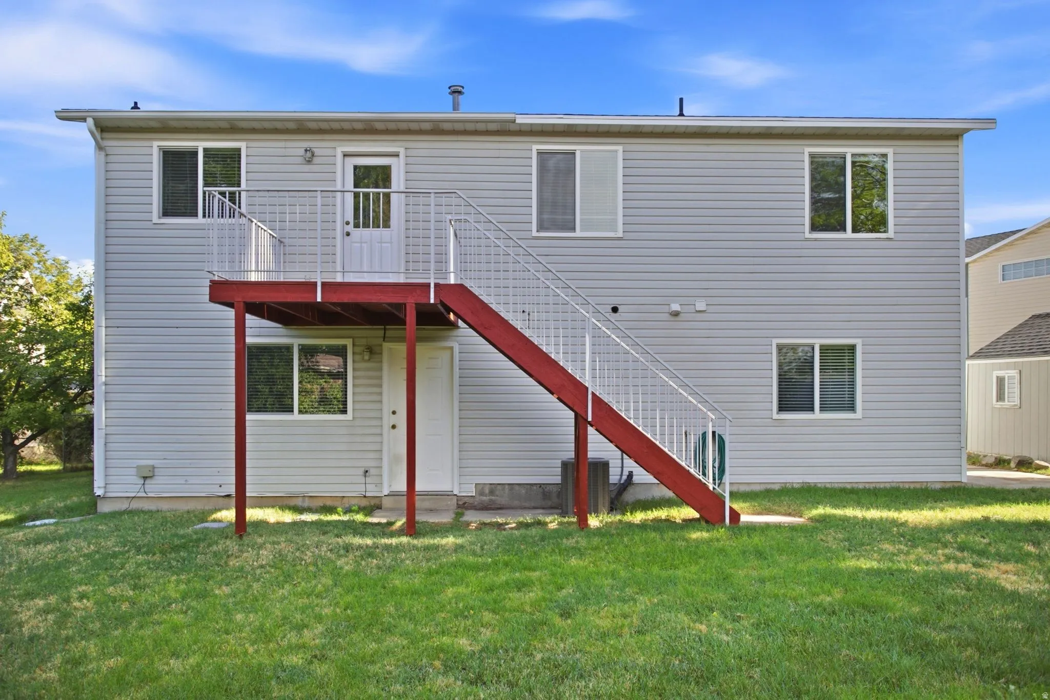 Rear exterior featuring light gray siding, multi-pane windows, a red exterior staircase, and an upper-level balcony with white railings