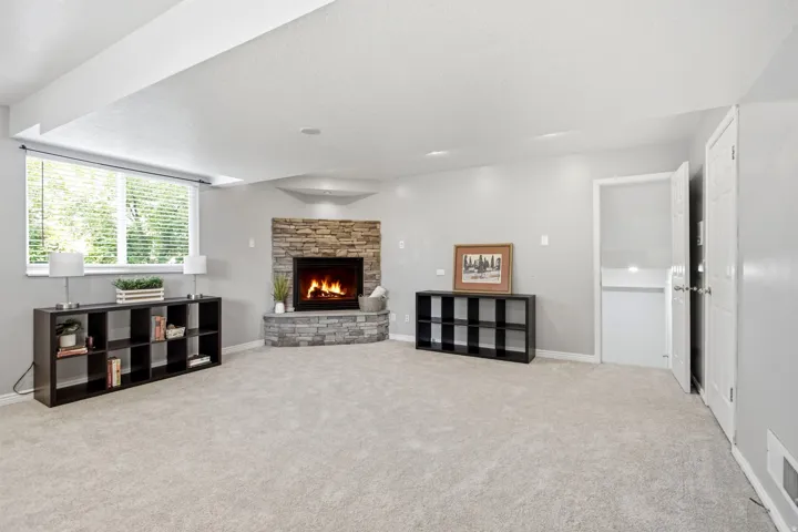 Corner fireplace featuring a stone surround and hearth, neutral carpeting, window with horizontal blinds, and recessed lighting