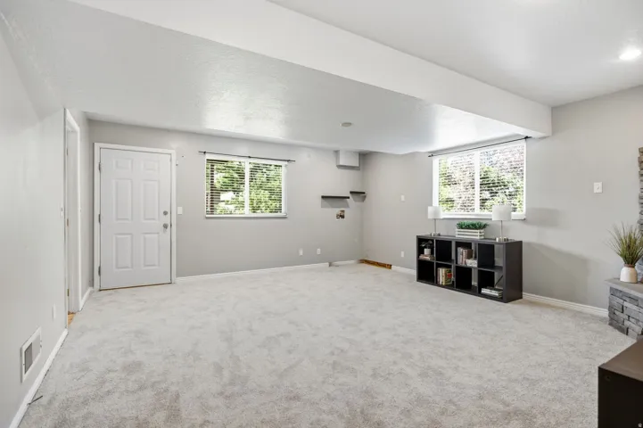 Bright, open recreation room featuring neutral carpeting, abundant natural light from multiple windows, white painted walls, and built-in shelving