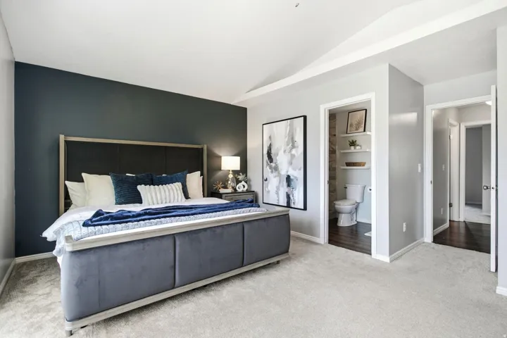 Vaulted ceiling, plush carpeting, dark accent wall, recessed lighting, and interior access to a bathroom with built-in shelving