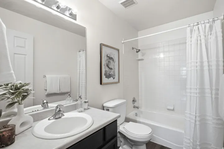 Bathroom featuring a vanity with an oval sink, chrome faucet, wall-mounted mirror, overhead lighting, and a white tiled shower-tub combination