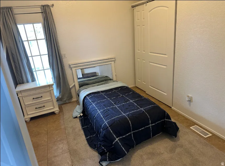 Bedroom space featuring a multi-pane window, tile flooring, and a sliding barn-door style closet