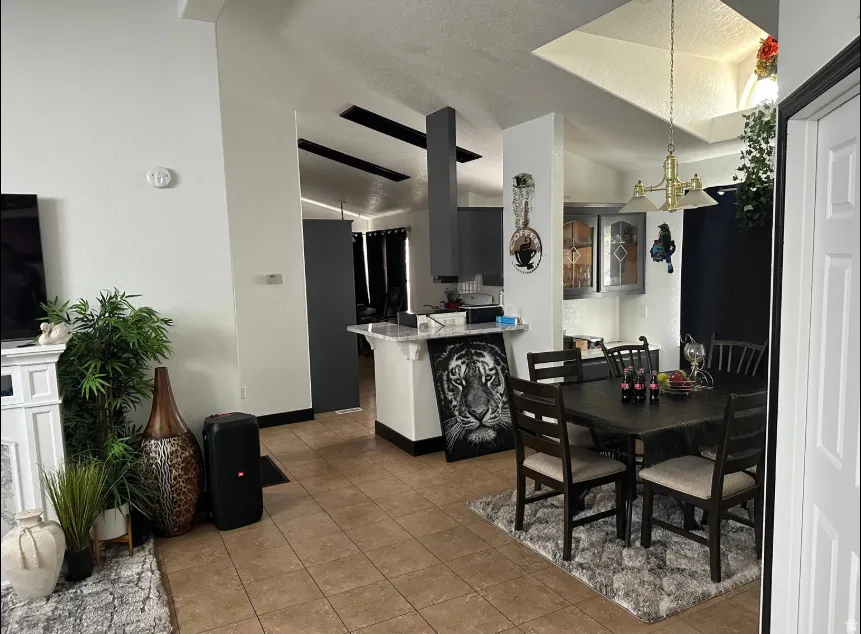 Open-concept living space featuring ceramic tile flooring, a dining area with a brass chandelier, and a kitchen pass-through with a light-colored countertop