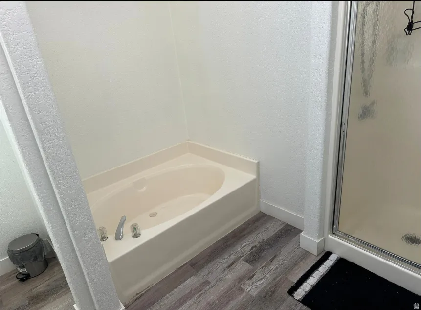 Soaking tub with chrome fixtures, wood-finish flooring, and white baseboards