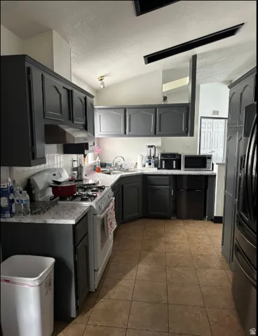 Kitchen featuring dark gray cabinetry, light-toned countertops, a white gas range, and warm-toned tile flooring