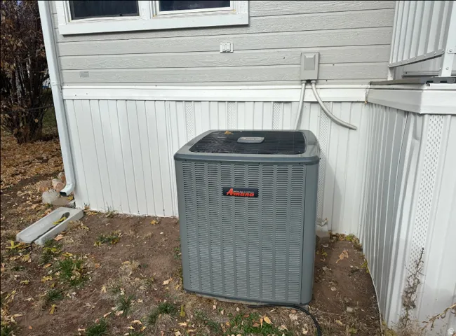 Exterior unit of a central air conditioning system, positioned beside the property with horizontal siding