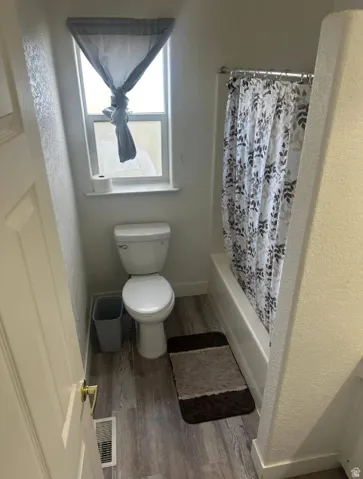 Bathroom featuring a full tub with shower, window, and wood-finish flooring