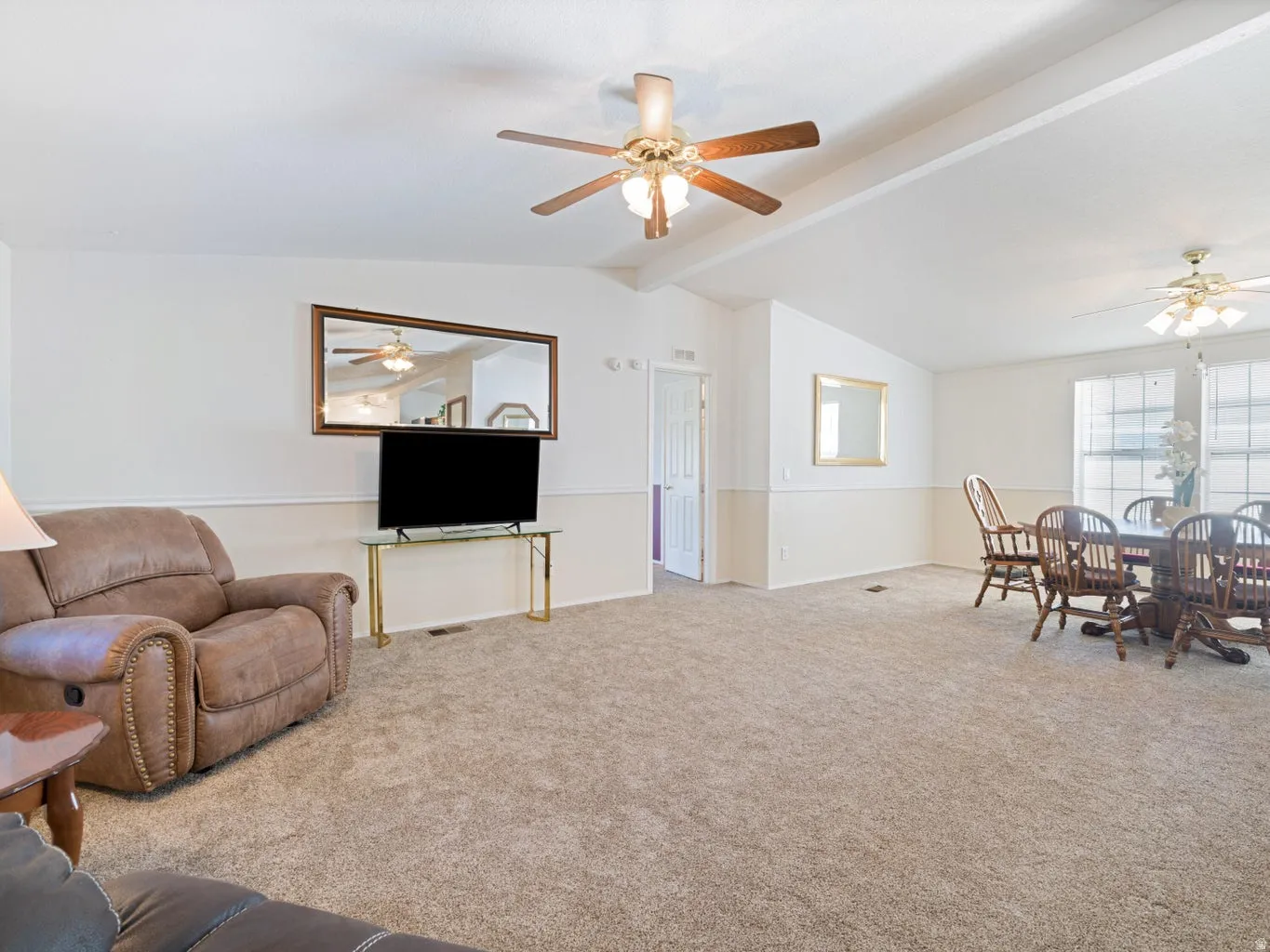 Open-concept living space featuring vaulted ceilings, ceiling fans with light fixtures, and neutral carpeting