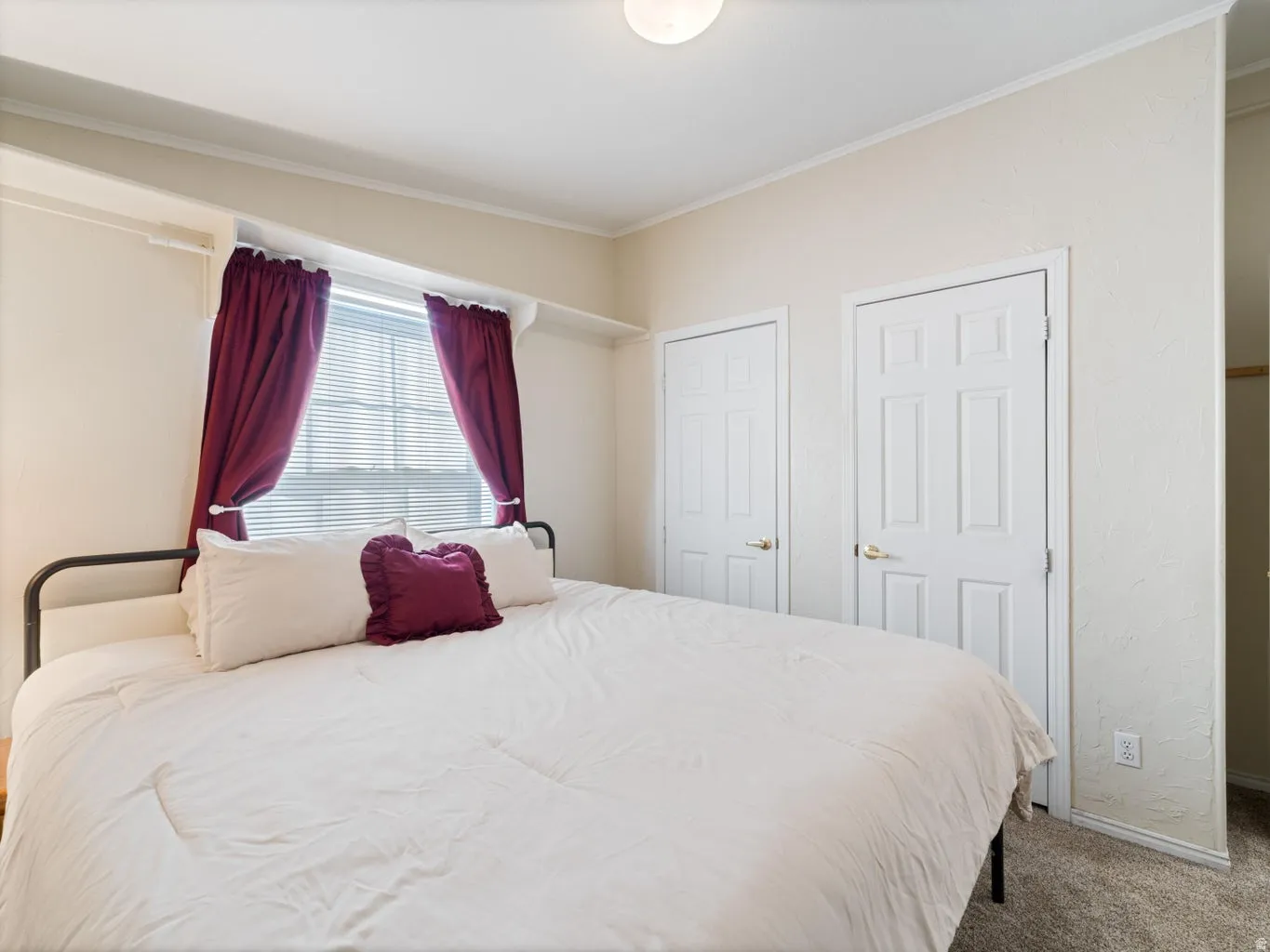Bedroom featuring a window with blinds, two paneled doors with brass hardware, ceiling-mounted lighting, and neutral-toned textured walls