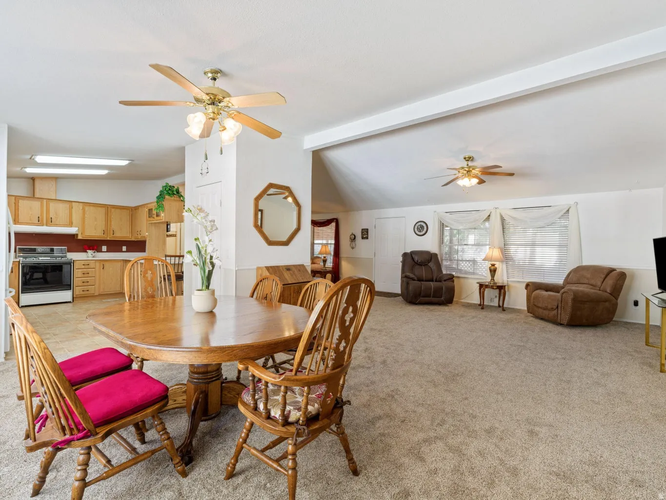 Open-concept living space featuring a kitchen with light wood cabinetry, a dining area with wood-finish flooring, and a carpeted living room