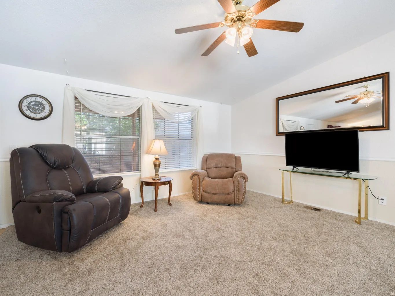 Spacious living area featuring neutral carpeting, a ceiling fan with integrated lighting, and white walls with wainscoting