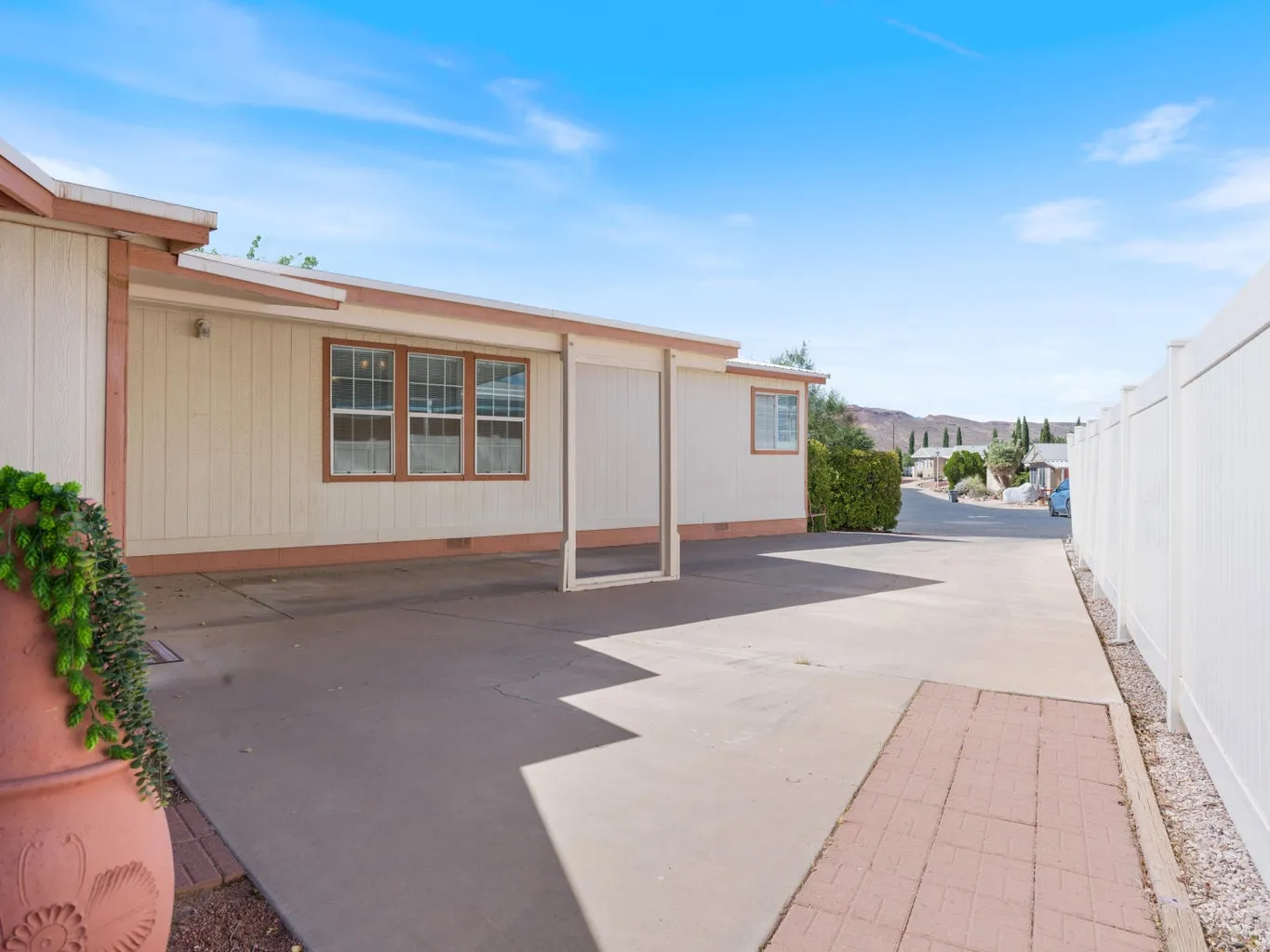 Exterior features include a tan facade with brown trim, covered parking area, concrete paving, and a white privacy fence