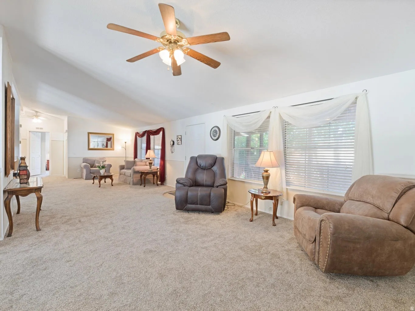 Spacious living area featuring vaulted ceilings, a ceiling fan with integrated lighting, and neutral carpet flooring