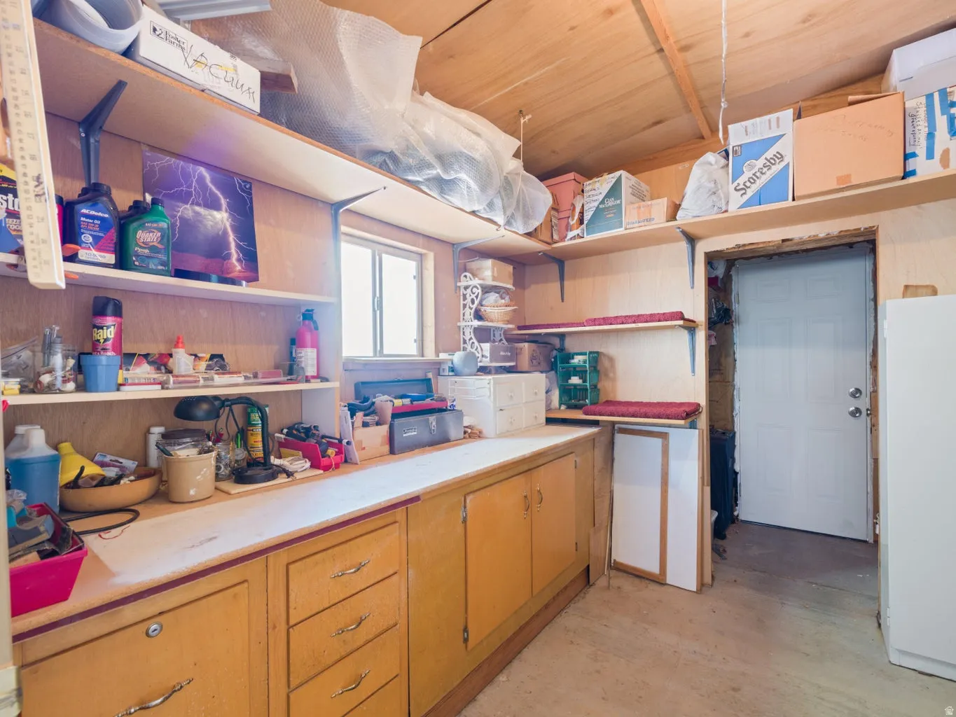 Utility room featuring built-in cabinetry, extensive shelving, a single window, and a light-colored door