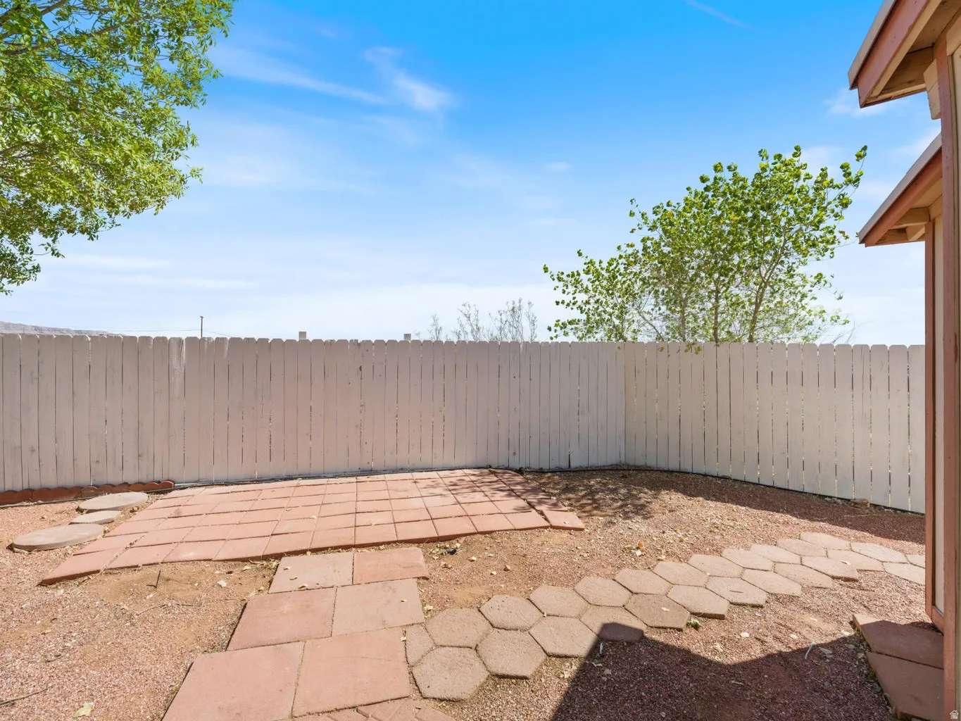 Enclosed backyard featuring a white picket fence, a red paver patio, and an irregular stone pathway