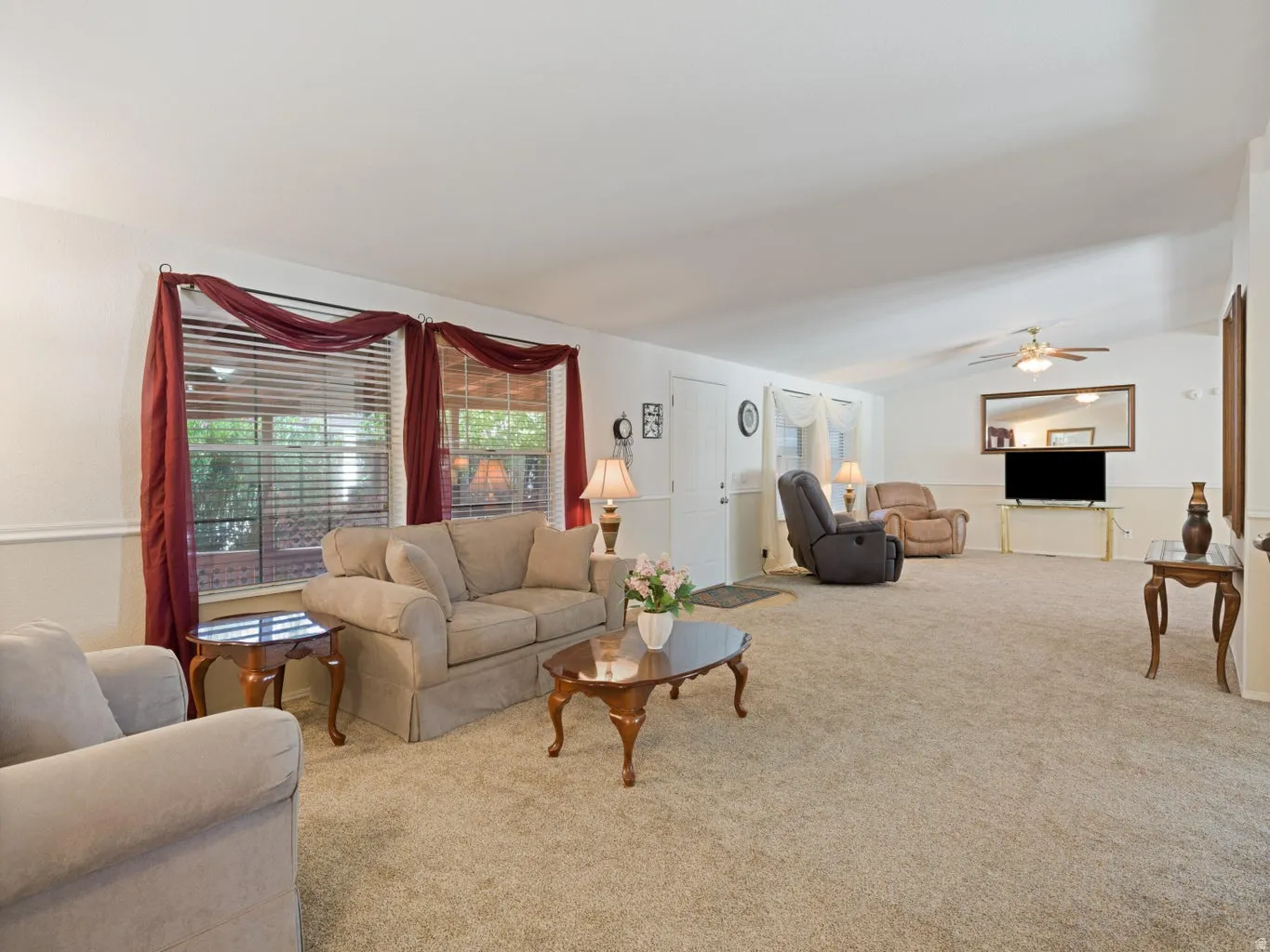 Spacious living area featuring neutral carpeting, a vaulted ceiling, and two large windows with blinds