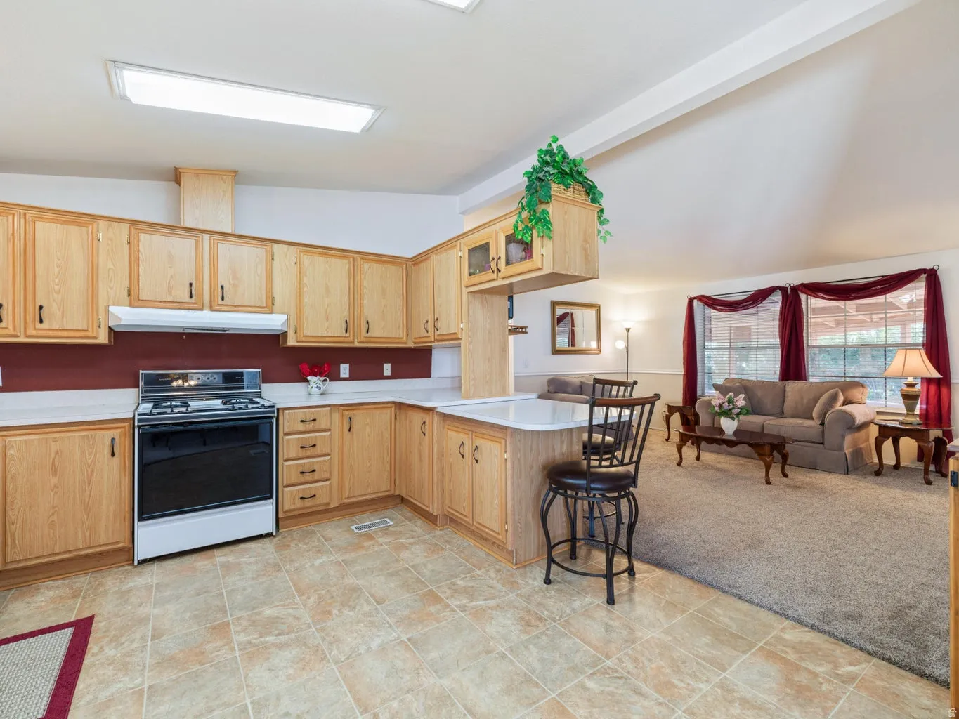 Open-concept kitchen with light wood cabinetry, a white gas range, and light tile flooring