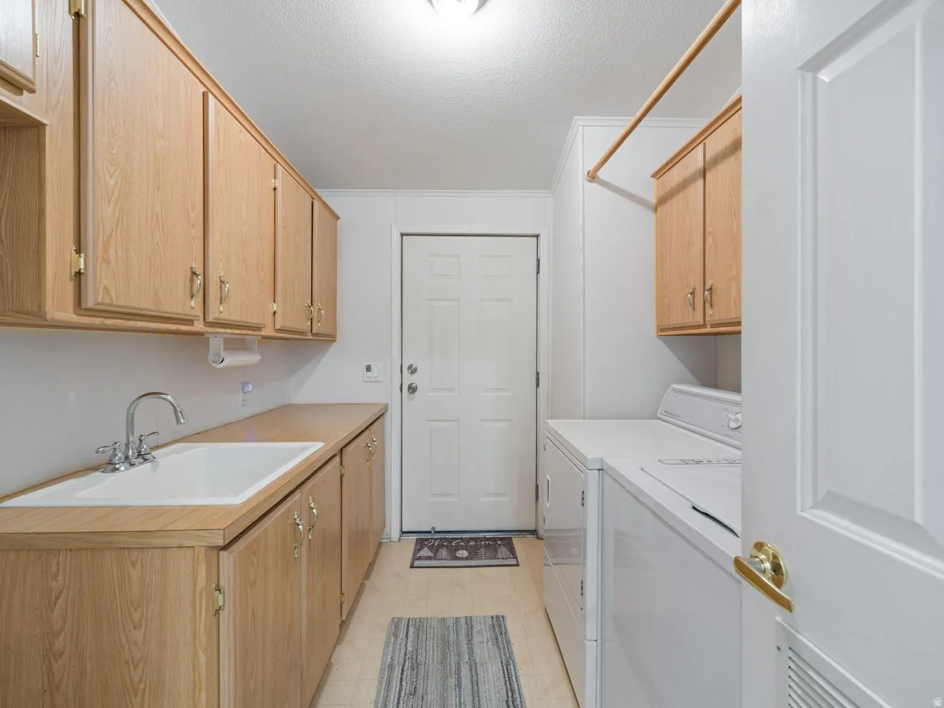 Utility room featuring extensive wood-finish cabinetry, a dedicated sink with a chrome faucet, and a clothes hanging rod