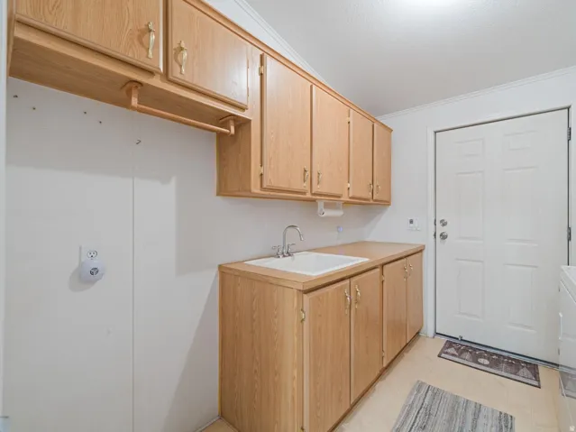 Utility room featuring wood-finish cabinetry, a built-in sink with a countertop, and light-toned flooring