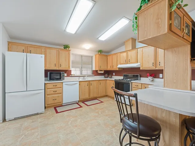 Kitchen featuring wood-finish cabinetry, solid surface countertops, a white appliance suite, tile flooring, and vaulted ceilings with recessed lighting