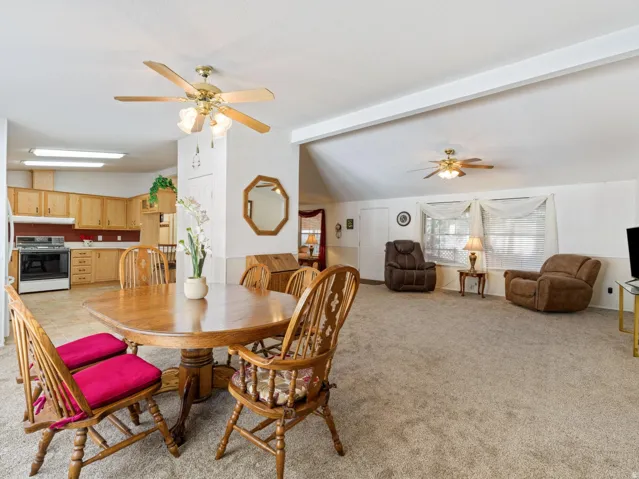 Open-concept living space featuring a kitchen with light wood cabinetry, a dining area with wood-finish flooring, and a carpeted living room