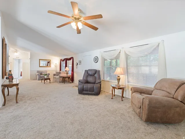 Spacious living area featuring vaulted ceilings, a ceiling fan with integrated lighting, and neutral carpet flooring