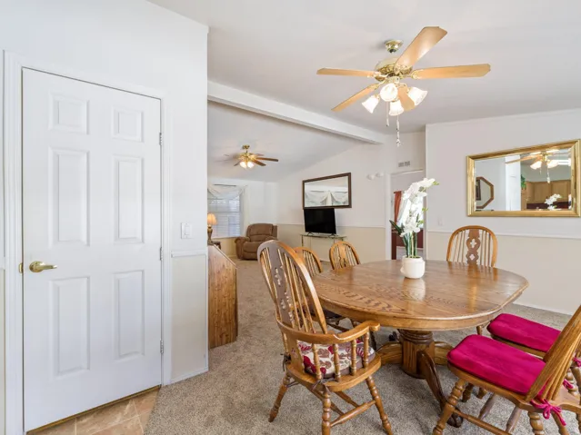 Carpeted dining area featuring a paddle fan with integrated lighting, a two-tone wall finish, and an adjacent tiled entryway