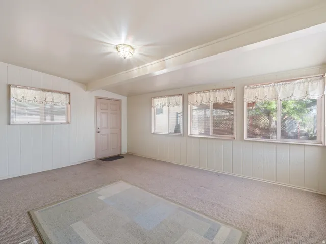 Room featuring light-toned carpeting, vertical plank wall paneling, a paneled entry door, and multiple windows