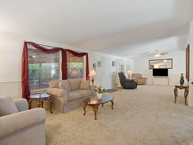 Spacious living area featuring neutral carpeting, a vaulted ceiling, and two large windows with blinds