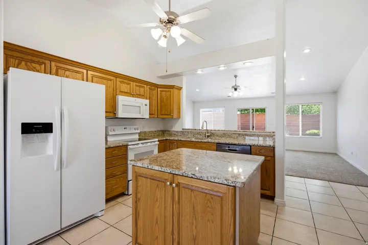 Kitchen featuring wood cabinetry, granite countertops, tile flooring, and a central island