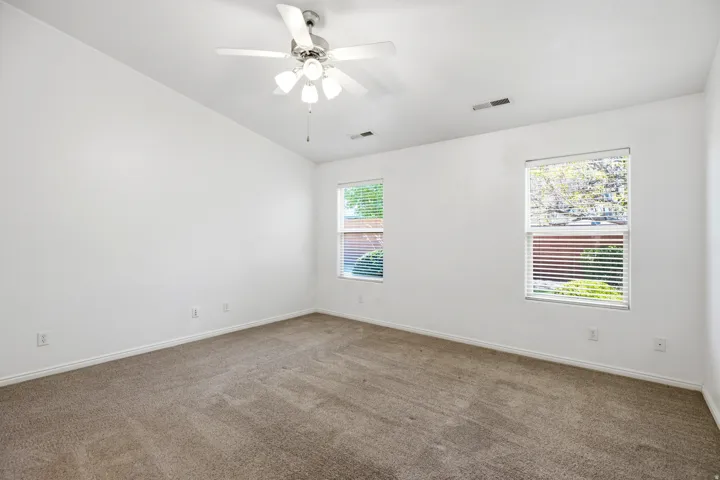 Spacious room featuring neutral carpet flooring, a ceiling fan with integrated lighting, and two windows with horizontal blinds