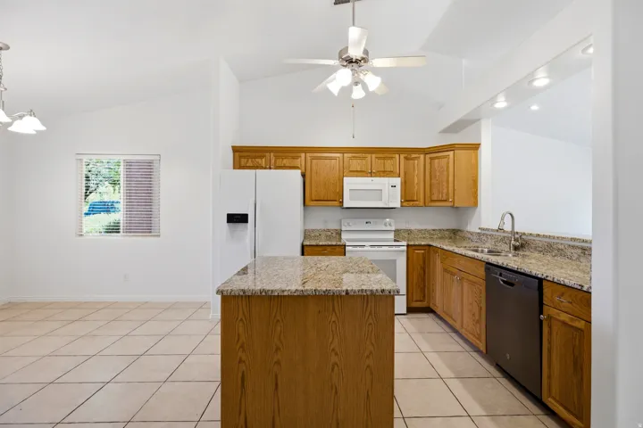 Kitchen featuring a central island with a stone countertop, wood cabinetry, and integrated white appliances