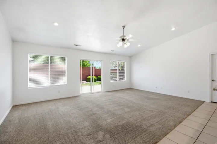 Spacious living area featuring neutral carpeting, a ceiling fan, recessed lighting, and a sliding glass door to the exterior
