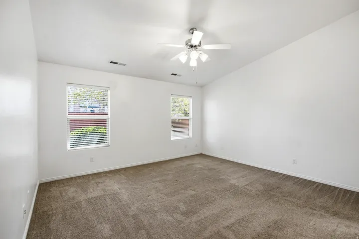 Spacious room featuring neutral carpet flooring, a vaulted ceiling, and two windows with blinds