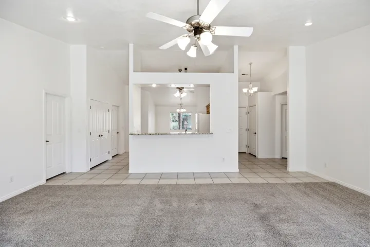 Spacious living area featuring grey carpet flooring, a white ceiling fan with integrated lighting, and recessed ceiling lights
