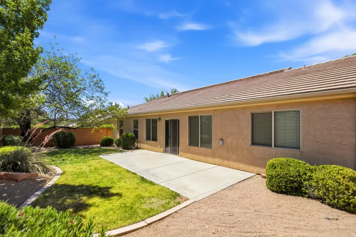 Expansive backyard featuring a concrete patio, a combination of green lawn and gravel landscaping, and mature trees providing natural shade