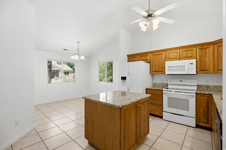 Kitchen featuring wood cabinetry, light-toned countertops, white appliances, and a central island